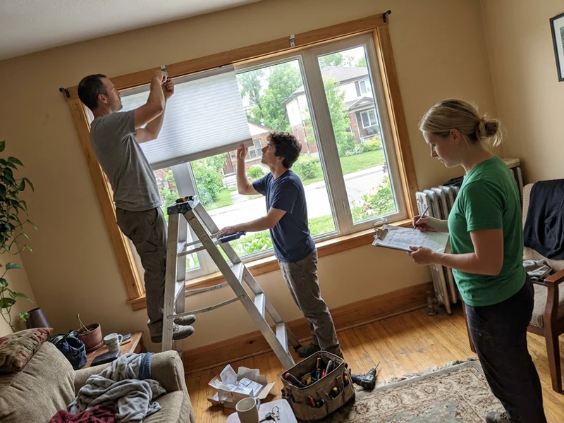 Two installers fitting a cellular shade headrail while a third checks the job sheet